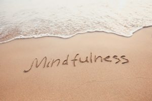 Waves lapping on the shore with the word Mindfullness written in the sand on the beach
