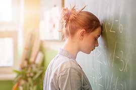 Photograph of A young woman with her eyes closed, leaning her head against a blackboard