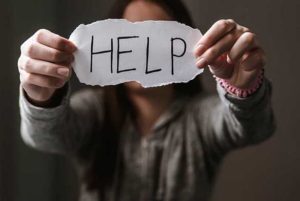 A young woman is holidng up a torn piece of paper with the word HELP on it