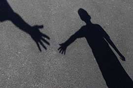 A shadow on the ground of an adult's hand reaching for a young person's outstretched hand