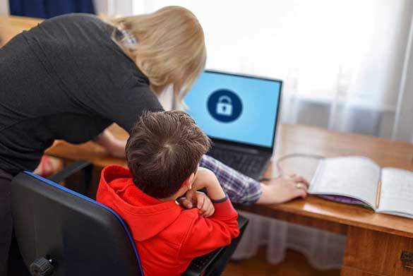 A young adult sitting in front of his laptop whilst an adult edits the parental settings