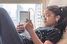 A young woman is relaxing and looking at her tablet with her headphones in