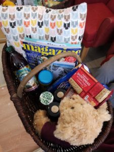 A hamper filled with a teddy bear, food, magazine and crafts