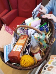 A hamper filled with a candle, wool, food, cards and crafts