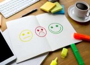 Printed smiley faces surrounded by highlighter pens, post-it notes and a cup of coffee