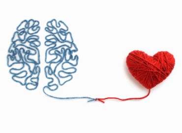 On a white background, to the left is a piece of blue wool laid down in the pattern and shape of a human brain, leading into the middle tied in a knot with a red piece of wool that leads off to the right to a heart shape made out of red wool.