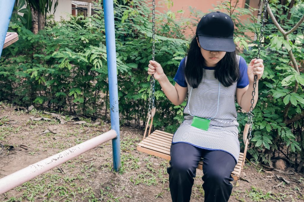 teenage girl sitting alone on a swing with cap covering her face