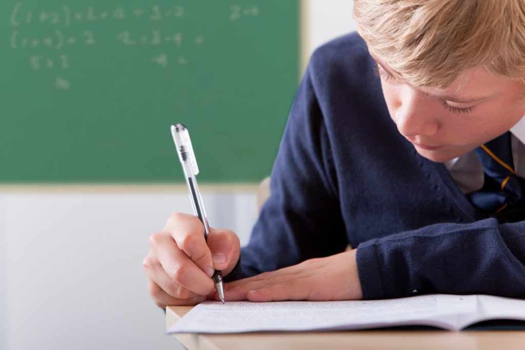 boy in school uniform at school desk handwriting in a notebook