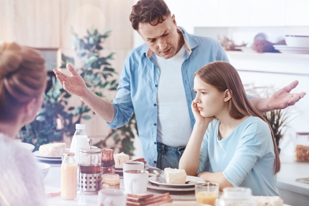 teenage girl at breakfast table being told off by her dad