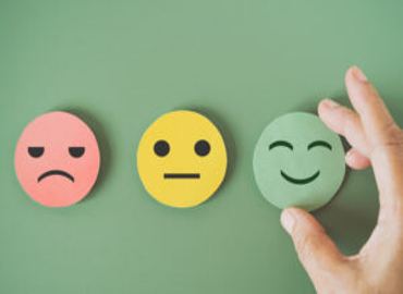 3 colored circles on a green background , one angry, one indifferent and a hand picking up the happy face