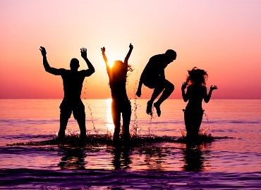 Four silhouettes jumping in sea at sunset